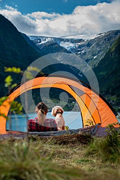 Traveling Norway, Young woman sits in the tent with her dog enjoying Beautiful view of Buerdalen Valley and Sandvevatnet Lake