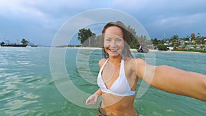 Traveling in Thailand. Pretty young woman in swimsuit taking selfie on the tropical beach.