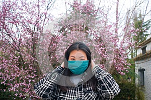 Traveling in virus times - young happy and beautiful Asian Chinese woman in face mask against covid19 enjoying sakura blooming