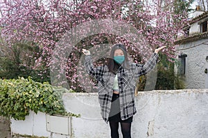 Traveling in virus times - young happy and beautiful Asian Japanese woman in face mask against covid19 enjoying sakura blooming