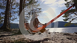 Traveling woman in a hat is resting in an orange hammock. beautiful view of the river and mountains. Norway telemark