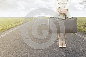 Traveling woman waits with her suitcase on the roadside photo