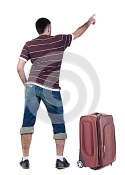 Traveling young man with suitcas pointing at wall.