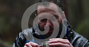 Traveling young tourist enjoying nature drinking hot tea while sitting in forest in rainy