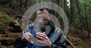 Traveling young tourist enjoying nature drinking hot tea while sitting in forest in rainy