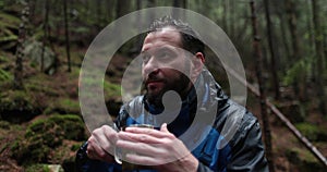 Traveling young tourist enjoying nature drinking hot tea while sitting in forest in rainy