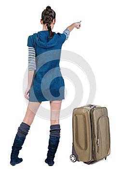 Traveling young woman in dress with suitcas pointing at wall