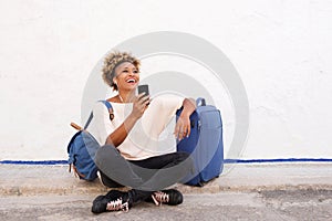 Traveling young woman sitting on sidewalk with suitcase and listening to music