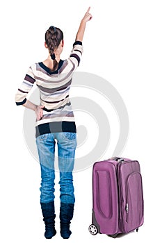 Traveling young woman with suitcas pointing at wall.