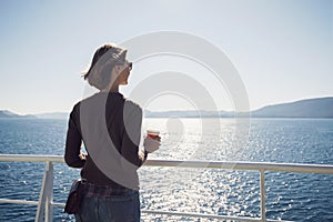 Traveller girl standing on ferry boat, looking at the sea and holding a coffee cup, travel and active lifestyle concept