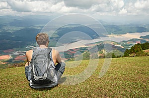 Traveller gray backpack resting enjoying the sunny valley of mountains in the background