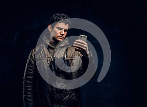 Traveller in hiking gear with binoculars uses GPS navigation on his smartphone in the studio against a dark wall