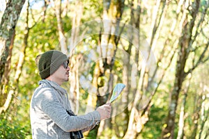 Traveller man who is wearing a sunglasses is looking at the map in the morning on vacation while he is traveling into the wild