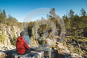 Traveller sits on a high rock and observes a beautiful natural lake in hiidenportti national park, Sotkamo in kainuu region,