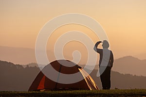 Traveller is standing by the tent during overnight camping while looking at the beautiful scenic sunset over the mountain for