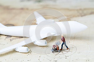 Traveller and transportation concept, miniature adult man with airport cart and luggage with toy airplane on vintage world map