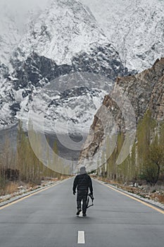 Traveller walking alone on the country road, hand holding camera with snow and rock mountain view. Travel lifestyle