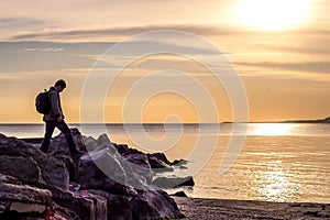 Traveller walking on rock cliff against sea, sunrise or sunset