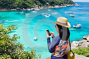 Traveller woman with colorful swimming suit use mobile take photo of view at top of mountain and speed boat in