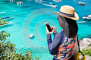 Traveller woman with colorful swimming suit use mobile take photo of view at top of mountain and speed boat in