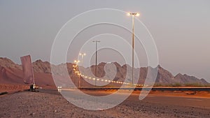 travelling by auto across desert, modern highway along mountains, illuminating lights in evening