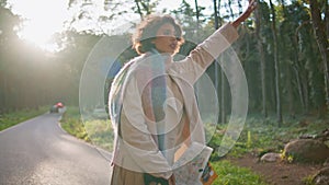 Travelling girl catching car on road sunlit forest holding map. Woman tourist