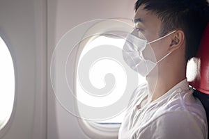 travelling man is wearing protective mask onboard in the aircraft, travel under Covid-19 pandemic, safety travels, social