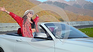 travelling in mountains by convertible car, young pretty woman standing and enjoying wind
