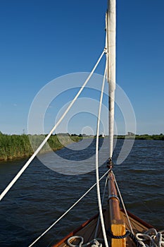 Travelling up a river from a moving sailing boat: foredeck and furled sails