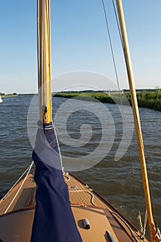 Travelling up a river from a moving sailing boat: foredeck and furled sails