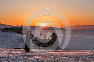 Travelling in winter at lake Baikal in Irkutsk, Russia. Winter landscape in sunset with young woman using mobile smart phone and e