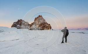 Travelling in winter, photographer carrying camera tripod at frozen lake Baikal in Siberia, Russia