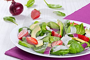 Trawberry, baby spinach, red onion, goat cheese and avocado salad on a white dish on a table mat