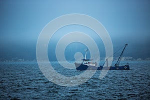 Trawler fishing boat sailing in open waters on a cold and foggy