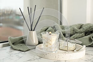 Tray with burning soy candle and beautiful bijouterie on white window sill indoors