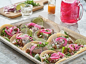 Tray of carne asada tacos topped with pickled onions and cojita cheese