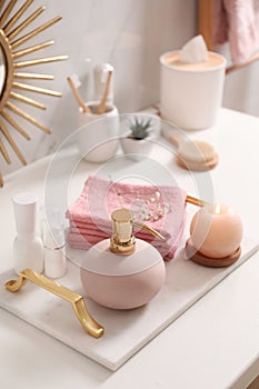 Tray with different toiletries, burning candle and towels on countertop in bathroom