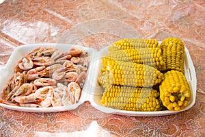 A tray is filled with corn and shrimp. Picnic outdoor