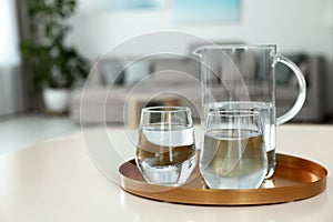 Tray with jug and glasses of water on white table in room. Refreshing drink