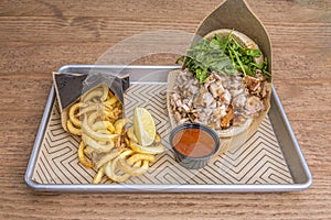 Tray with a large sandwich of chopped grilled meat, rocket in quantity and a portion of French fries