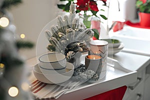 Tray with little Christmas tree, candle and dishware on kitchen counter