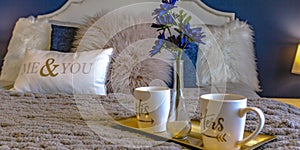 Tray with mugs and flower vase on top of a bed