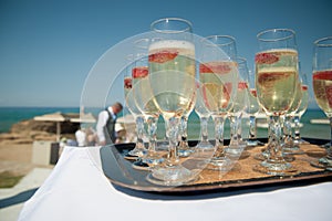 A tray of sparkling wine with strawberries by the beach, wedding