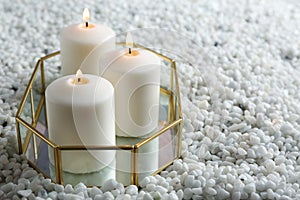Tray with three white burning candles on rocks.