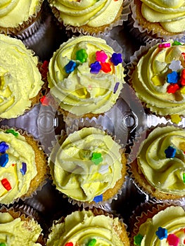 A tray of yellow icing cupcakes with sprinkles