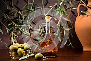 Trdition Crete flavored olive oil with spieces rosemary and pepper in local vial, with olives, clay jug and olive leafs on wooden