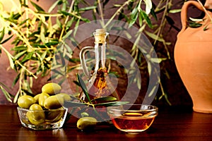 Trdition Crete flavored olive oil with spieces rosemary and pepper, with olives, clay jug and olive leafs on wooden background.