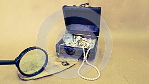 a treasure chest and an old map on a light next to a magnifying glass. there are pearls and shells in the box. search