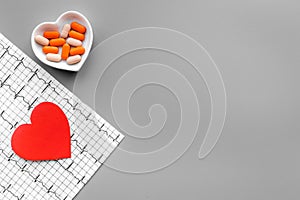 Treat heart. Pills in bowl in shape of heart and cardiogram on grey background top view copyspace photo