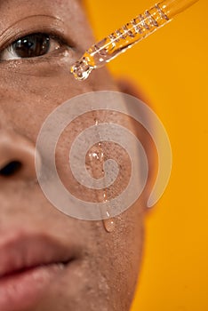 Treat your skin. Close up portrait of young asian man applying gel serum on his face using glass pipette isolated over